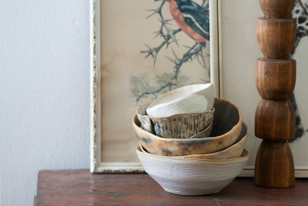 Handmade ceramic bowls stacked on a wooden table beside framed art