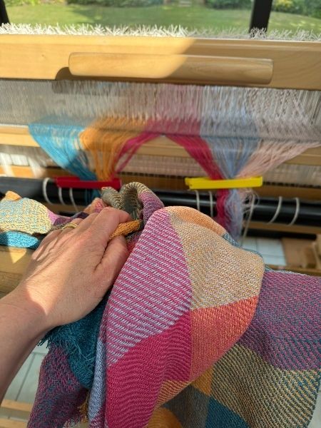 Hand weaving a colorful natural-fiber textile on a wooden loom